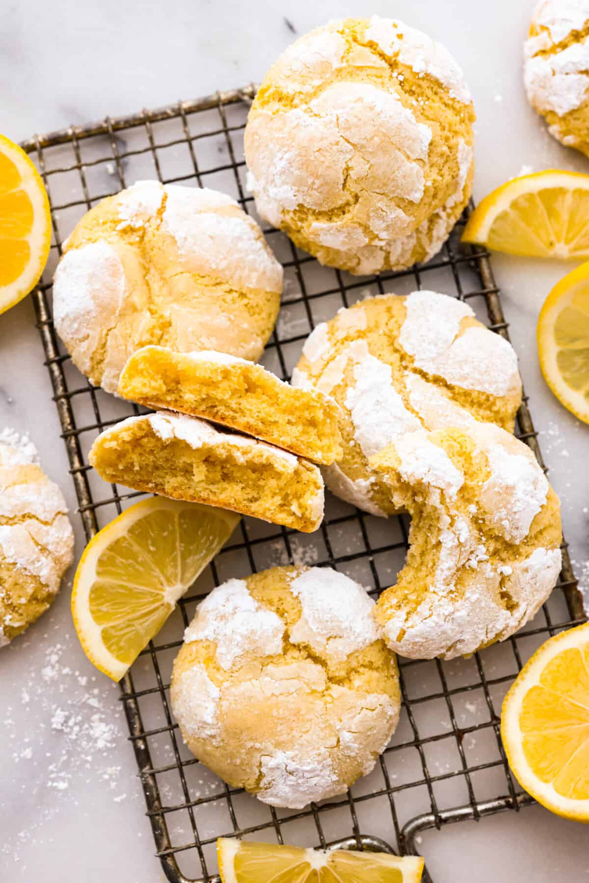 The crinkle cookies on a wire rack. Some have a bite taken out of them or are broken in half. - Lemon Crinkle Cookies