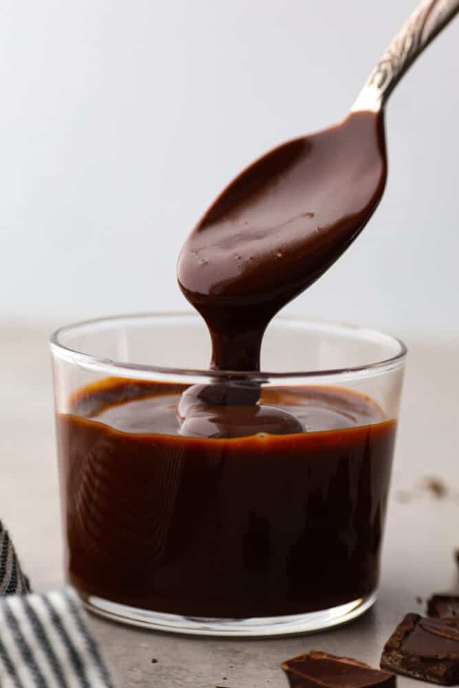 Chocolate ganache in a glass container with a spoon taking a scoop out. - Easy Chocolate Ganache