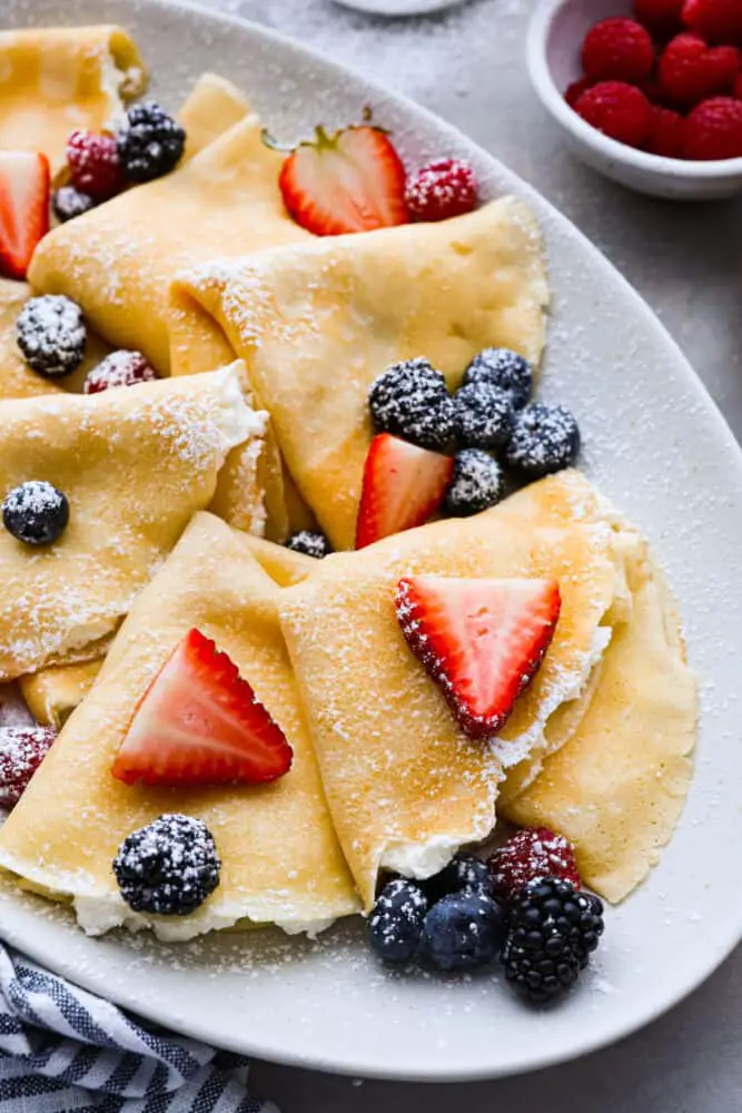 Close up of folding crepes on a gray platter. The crepes are dusted with powdered sugar and topped with berries. - Perfect Crepes
