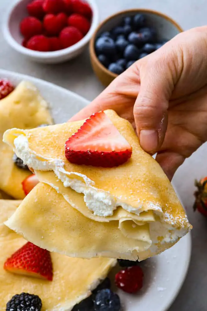 A folded crepe being held with filling on the inside and berries on top. - Perfect Crepes