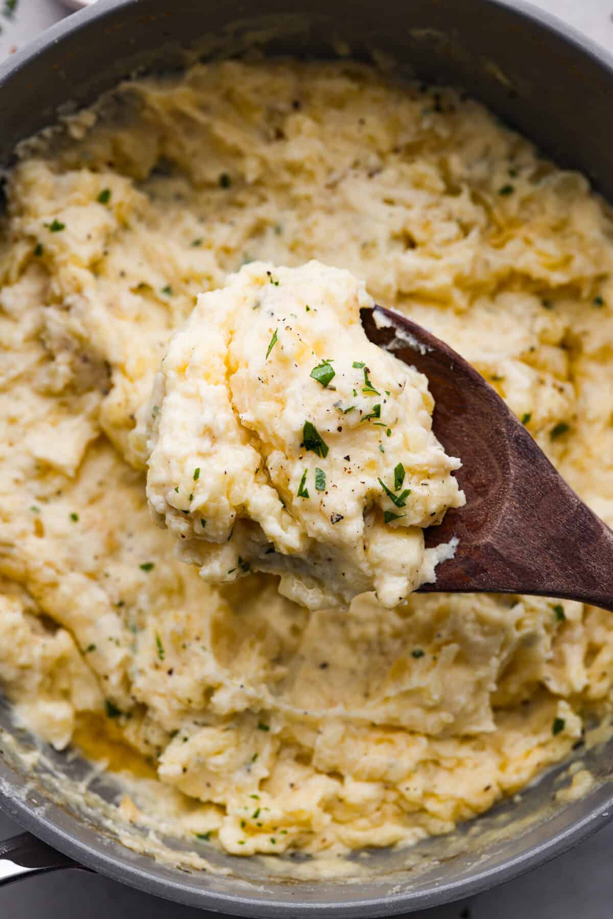 Close view of a wood serving spoon lifting a the mashed potatoes. - Boursin Mashed Potatoes