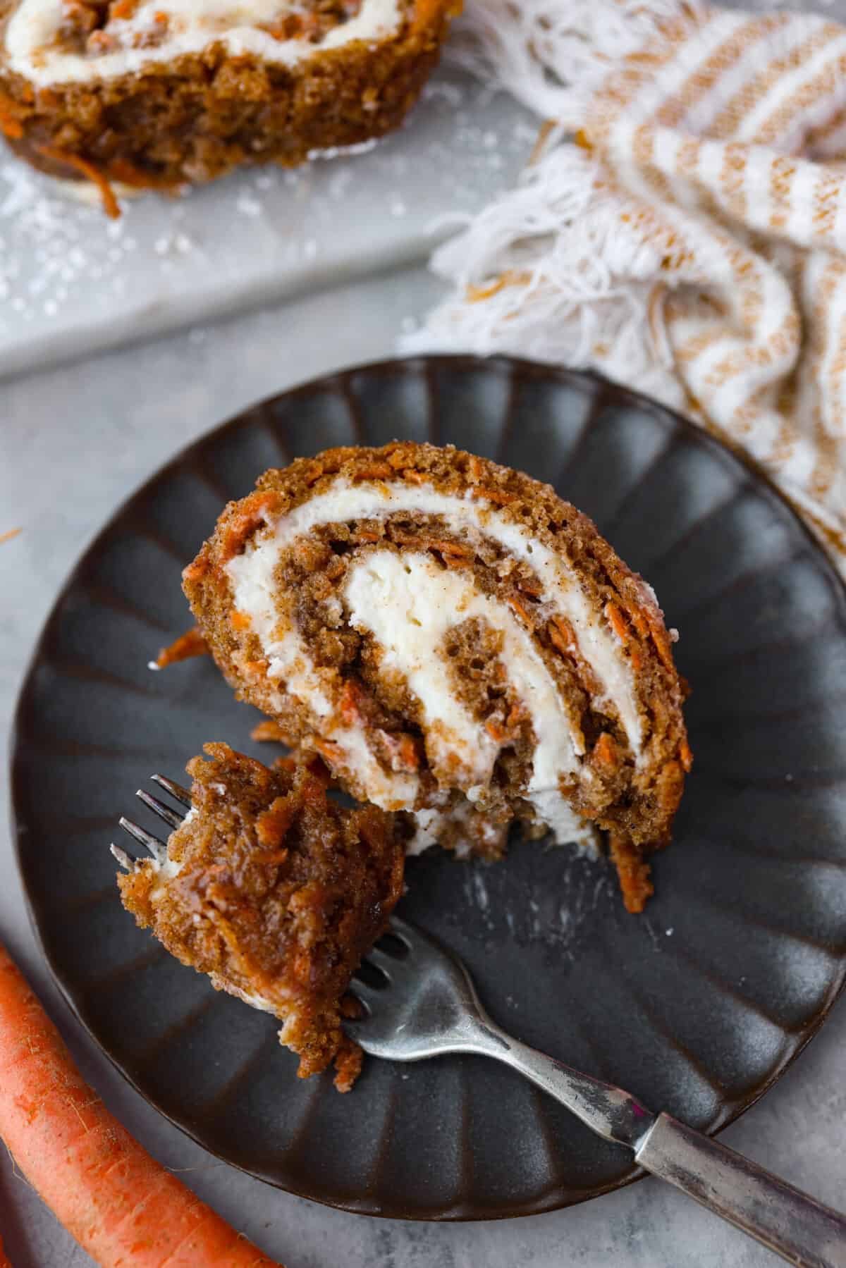 Taking a bite of cake that was served on a black plate. - Carrot Cake Roll