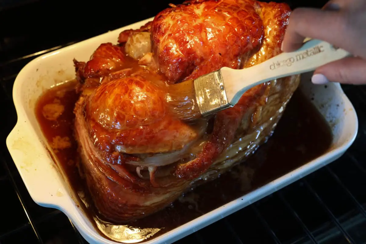 A honey baked ham with more glaze being added to it. - Classic Honey Glazed Ham