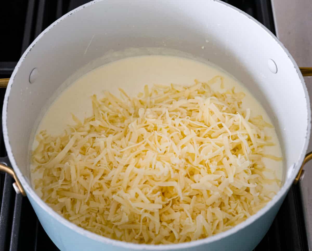 The cheesy sauce being melted together in a large pot. - White Cheddar Mac And Cheese