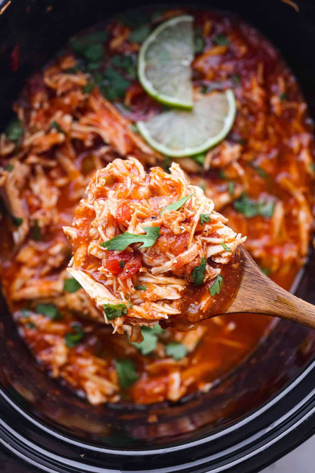 Close view of a serving spoon lifting chicken from the slow cooker. - Crockpot Salsa Chicken