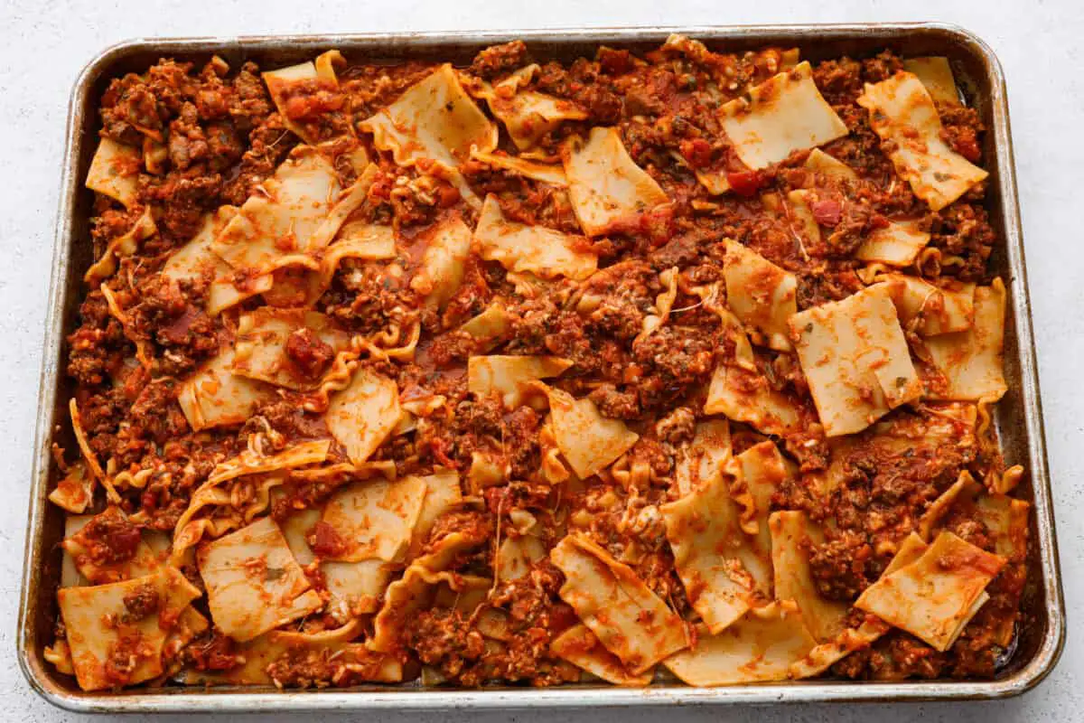 Lasagna noodles and meat being spread on a sheet pan. - Easy Sheet Pan Lasagna