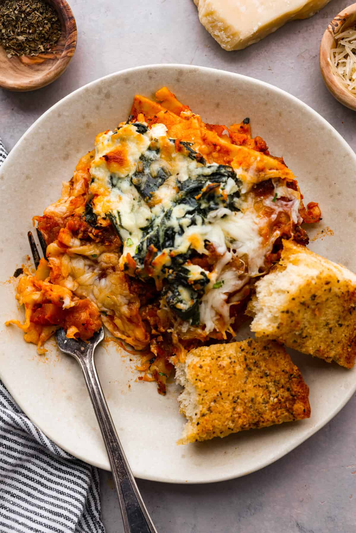 A small plate with a slice of lasagna and some garlic bread. - Easy Sheet Pan Lasagna