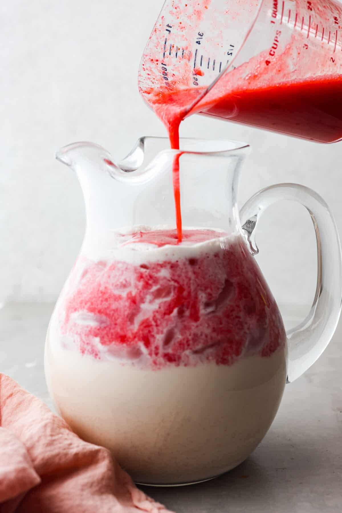 Close view of a large glass pitcher full of horchata with the strawberry puree pouring in. - Strawberry Horchata
