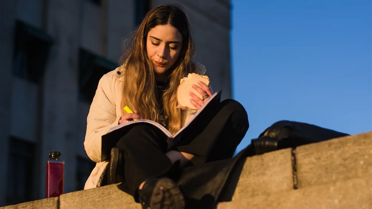young woman eating a sandwich and studying - The Ol' College Cry: Dealing With Student Stress