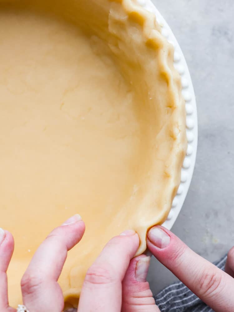 Close up of pie crust with hands crimping the edges. - Butter Pie Crust