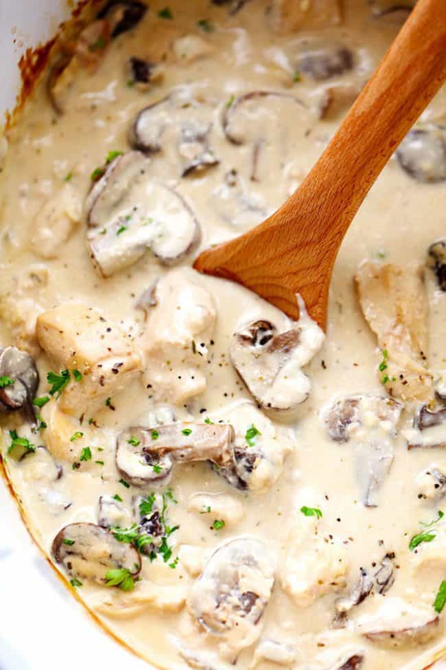 Chicken and mushroom stroganoff in a slow cooker with a wooden spoon stirring it. - Slow Cooker Chicken And Mushroom Stroganoff