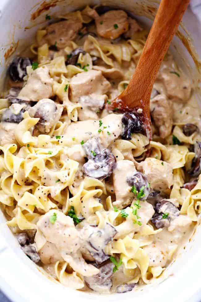 Chicken and mushroom stroganoff in a slow cooker being stirred by a wooden spoon. - Slow Cooker Chicken And Mushroom Stroganoff