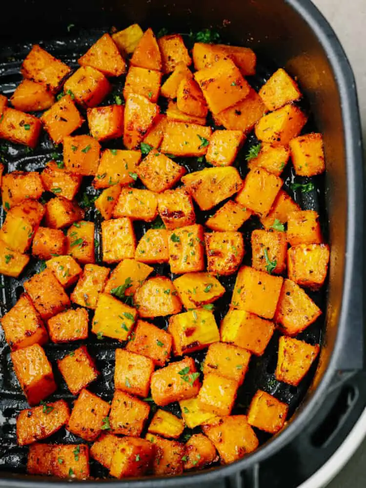 Top view of butternut squash in the air fryer and garnished with fresh chopped parsley. - Air Fryer Butternut Squash