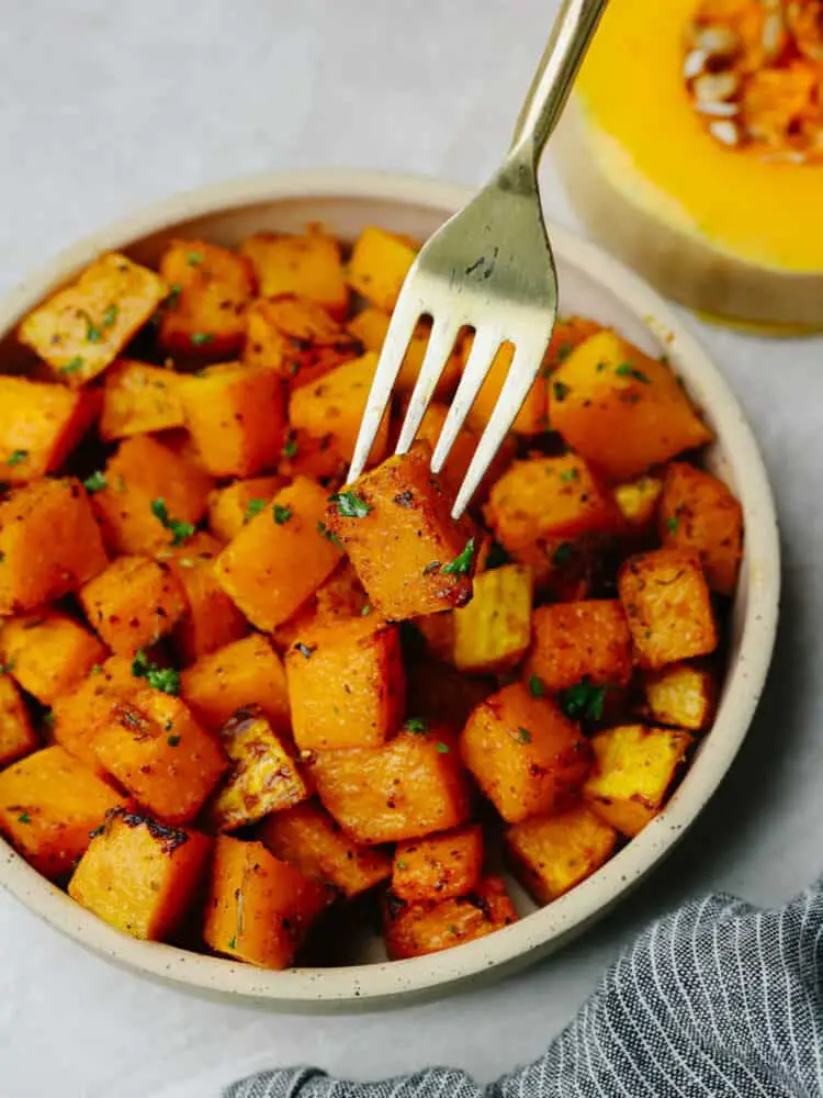 Close up photo of squash on a small tan colored plate with a fork lifting out a piece of squash. - Air Fryer Butternut Squash