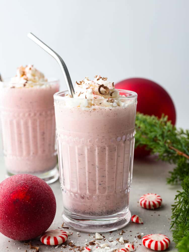 2 glasses of peppermint milkshakes surrounded by red Christmas ornaments and  pine tree branches. - Copycat Chick-Fil-A Peppermint Milkshake
