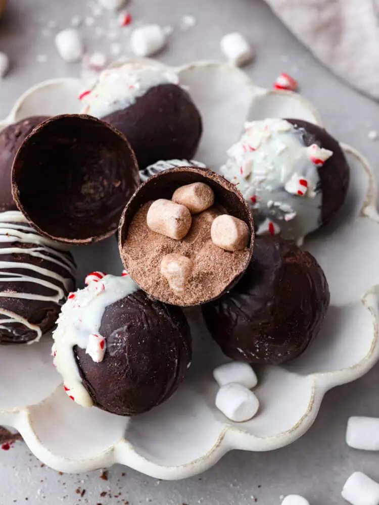 Hot chocolate bombs stacked on a serving dish. One is split in half so the cocoa powder and marshmallow filling can be seen. - Homemade Hot Chocolate Bombs