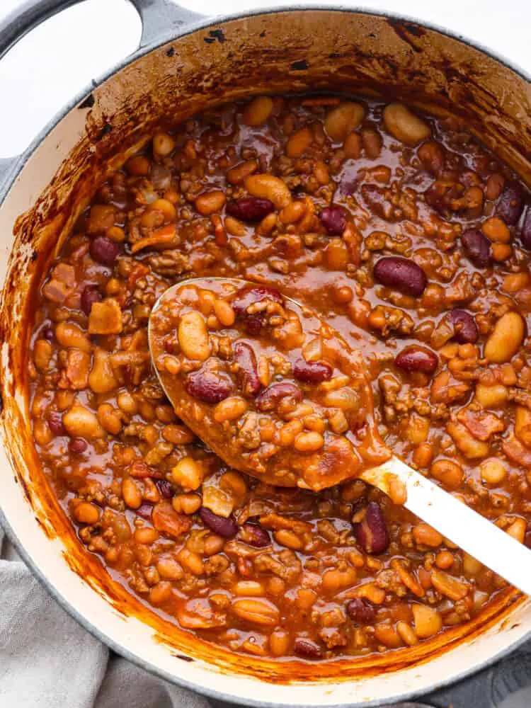 Hero image of cowboy beans in a blue and white pot. A white serving spoon is scooping some up. - Amazing Cowboy Beans