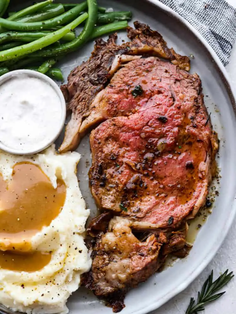 A slice of prime rib served with sauce, mashed potatoes and gravy, and broccolini. - Insanely Delicious Prime Rib Recipe