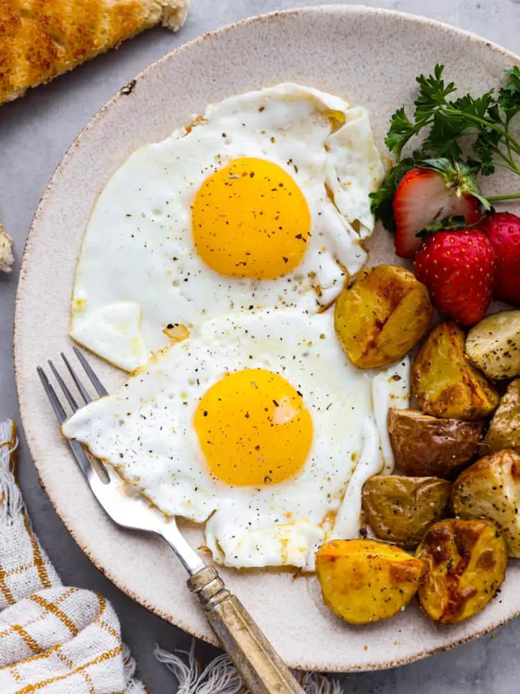 A plate of food with eggs, potatoes, and strawberries with a fork. - Sunny Side Up Eggs