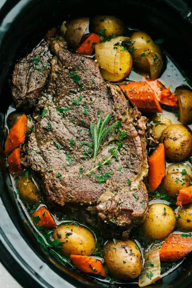 Top-down view of pot roast and vegetables in a slow cooker. - Melt In Your Mouth Pot Roast Recipe