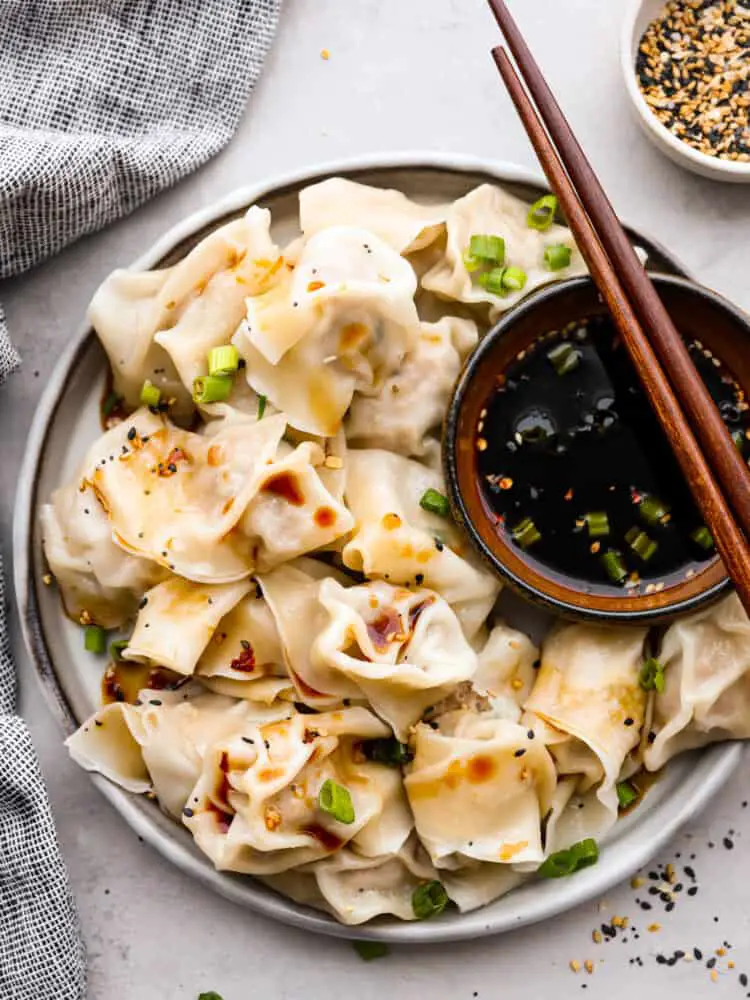 Top-down view of boiled wontons served on a white plate with soy sauce. - Pork Wontons