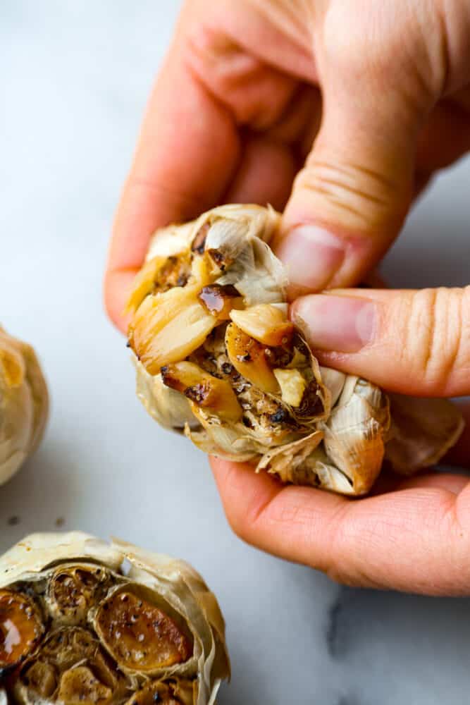 A garlic head being torn open to reveal the cloves inside. - Roasted Garlic