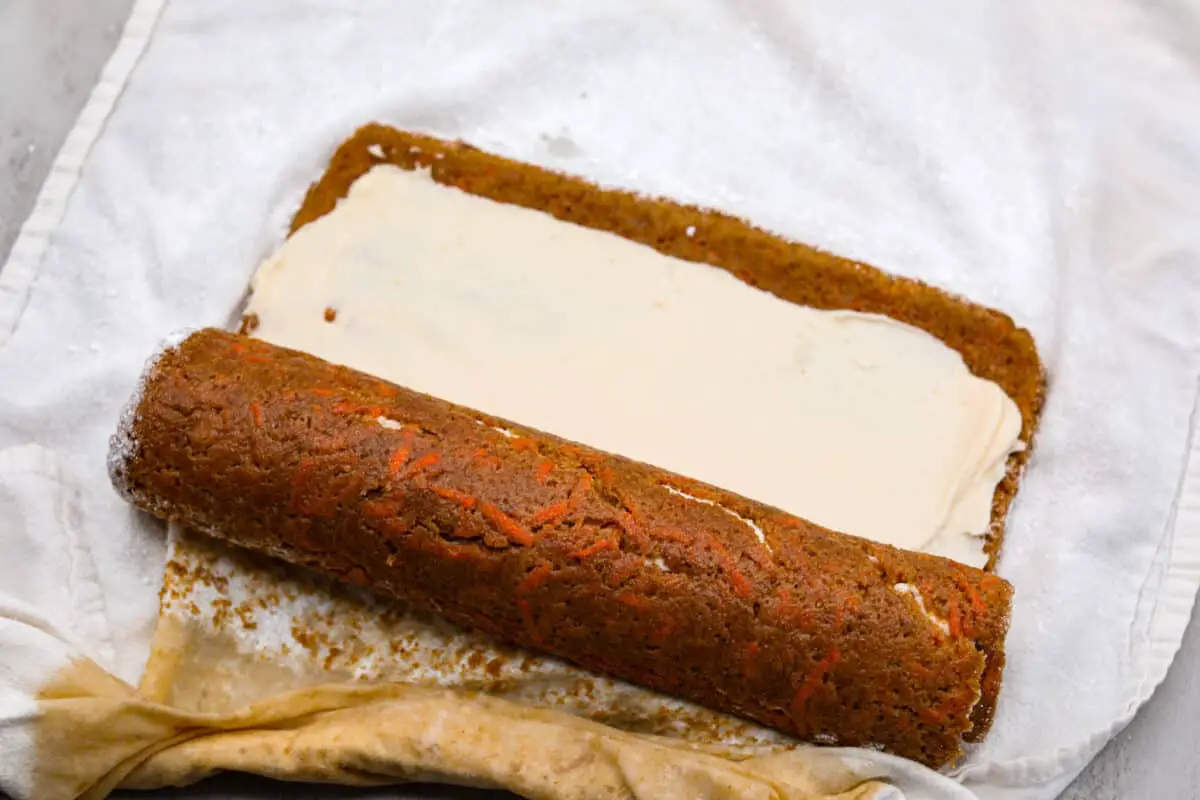Rolling up the cream cheese filled carrot cake. - Carrot Cake Roll