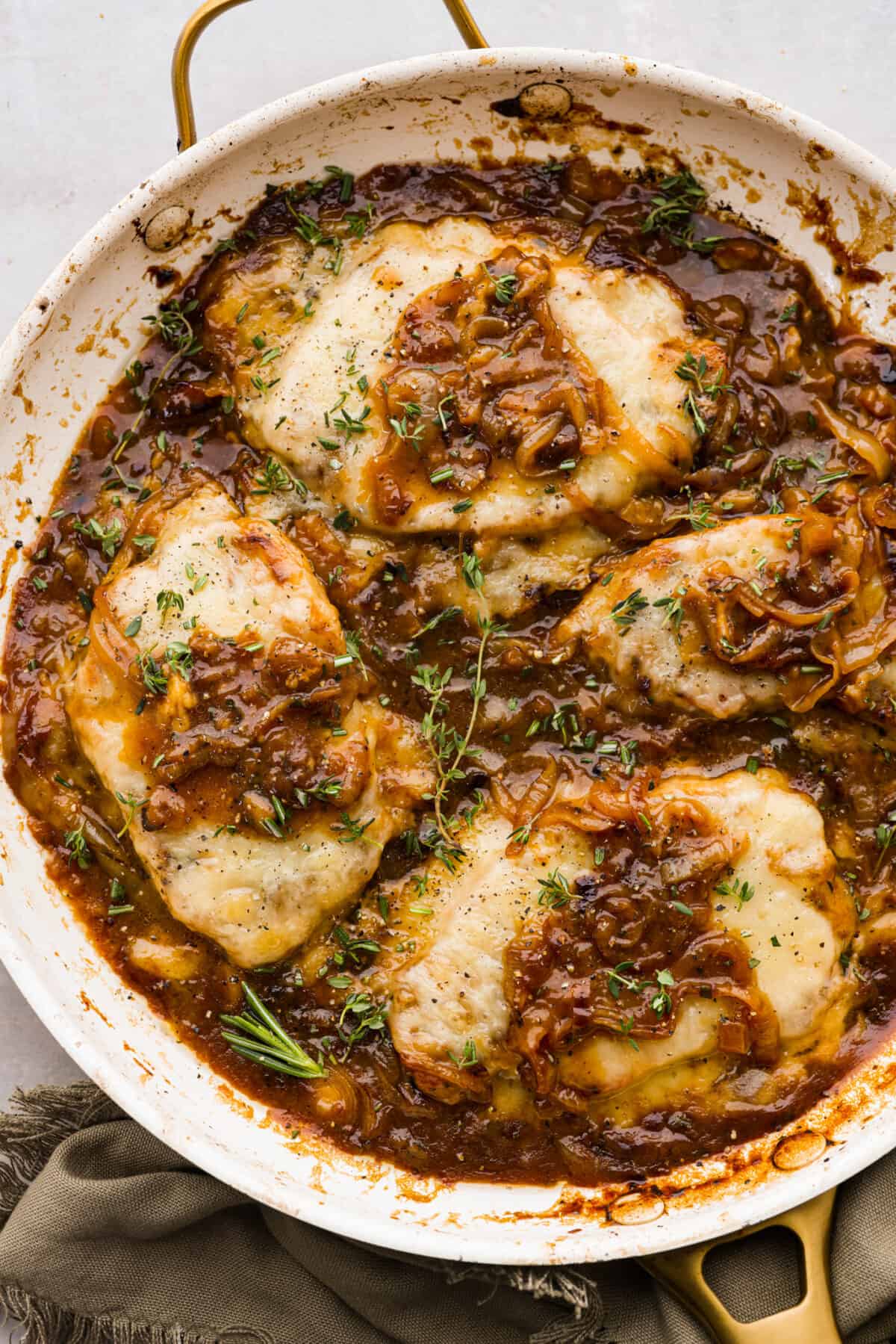 4 pork chops in a skillet topped with cheese and onion gravy. - French Onion Pork Chops