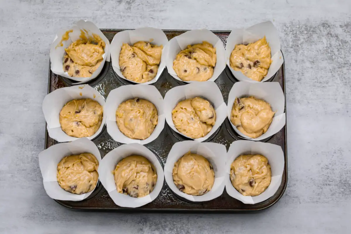 Chocolate chip muffin batter in a muffin tin filled with white muffin liners. - Banana Chocolate Chip Muffins